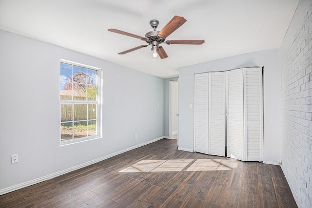 unfurnished bedroom featuring brick wall, wood finished floors, a ceiling fan, baseboards, and a closet