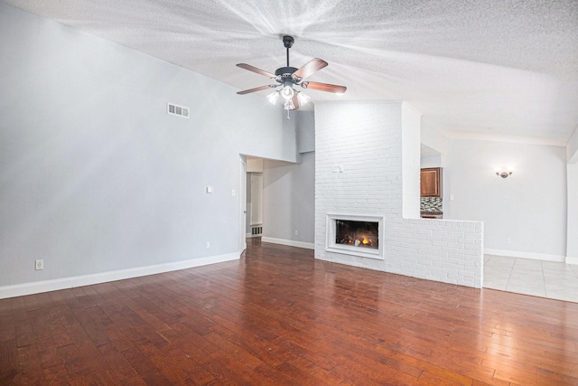 unfurnished living room with ceiling fan, a fireplace, a textured ceiling, and light wood-type flooring