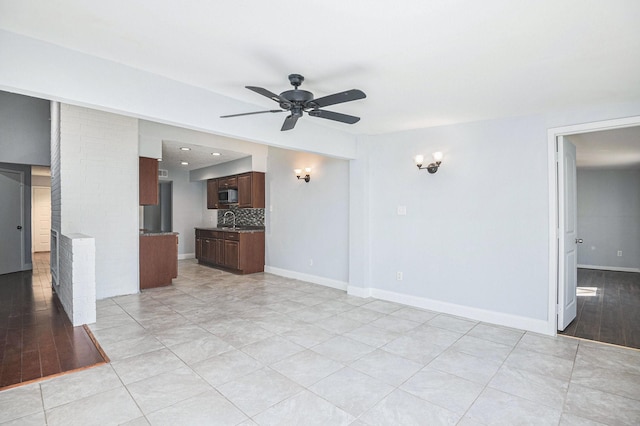 empty room with light tile patterned flooring, a sink, a ceiling fan, and baseboards