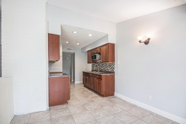 kitchen featuring stainless steel microwave, backsplash, a sink, a textured ceiling, and baseboards