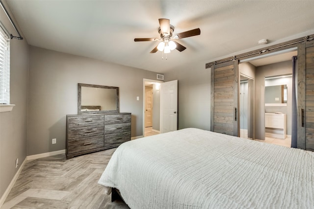 bedroom featuring ceiling fan, ensuite bathroom, a barn door, and light parquet floors