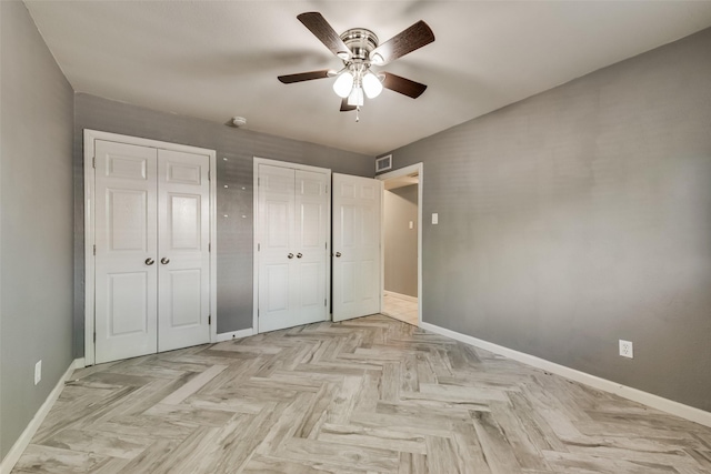 unfurnished bedroom with ceiling fan, light parquet flooring, and multiple closets