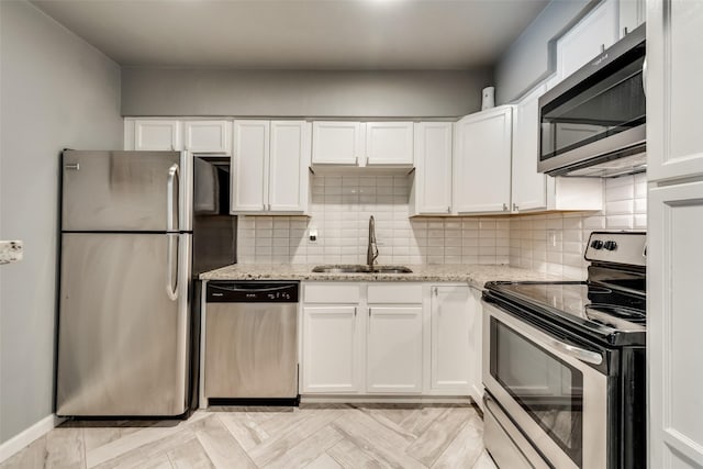 kitchen featuring appliances with stainless steel finishes, white cabinetry, light stone counters, and sink