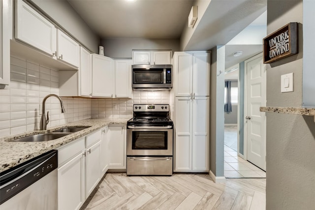 kitchen featuring appliances with stainless steel finishes, light parquet flooring, white cabinets, light stone counters, and sink