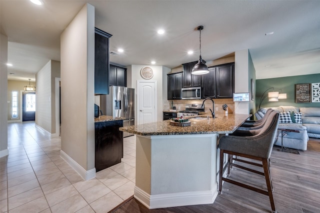 kitchen featuring light stone countertops, stainless steel appliances, kitchen peninsula, pendant lighting, and decorative backsplash