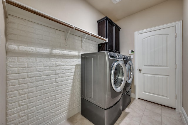 clothes washing area with washer and clothes dryer, cabinets, light tile patterned floors, and brick wall