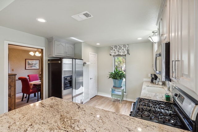 kitchen with light stone countertops, light hardwood / wood-style flooring, a chandelier, gray cabinets, and appliances with stainless steel finishes