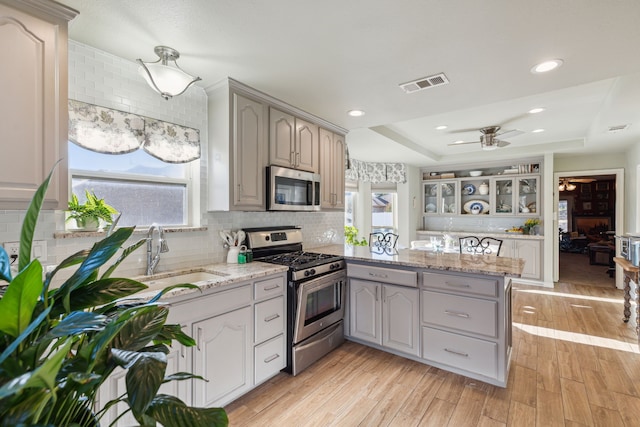 kitchen with stainless steel appliances, a raised ceiling, sink, light hardwood / wood-style flooring, and gray cabinets