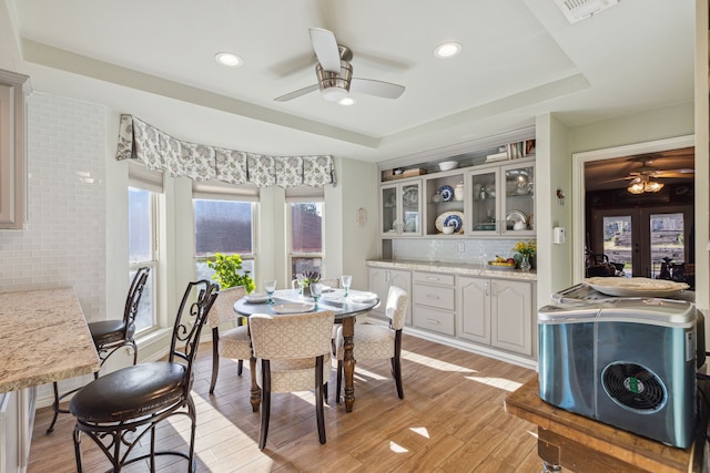 dining space featuring ceiling fan, french doors, a tray ceiling, and light hardwood / wood-style flooring