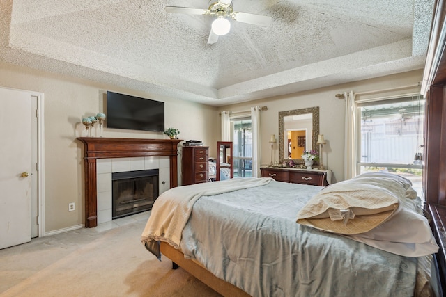 carpeted bedroom featuring a tray ceiling, a tiled fireplace, ceiling fan, and a textured ceiling