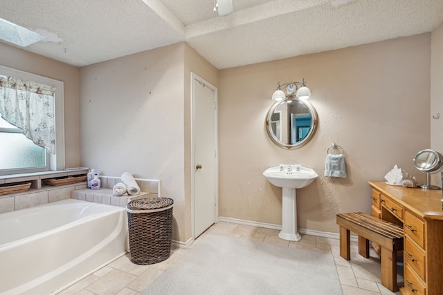 bathroom with sink, a skylight, tile patterned flooring, a tub to relax in, and a textured ceiling