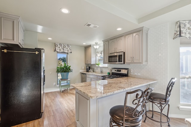 kitchen featuring stainless steel appliances, light stone counters, kitchen peninsula, light hardwood / wood-style floors, and decorative backsplash