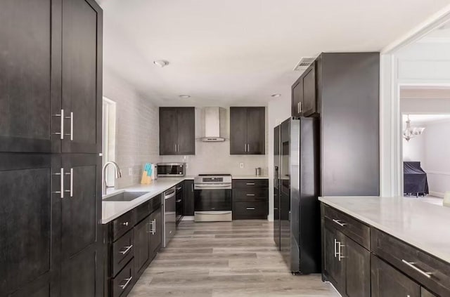 kitchen with dark brown cabinetry, stainless steel appliances, wall chimney range hood, sink, and light hardwood / wood-style flooring