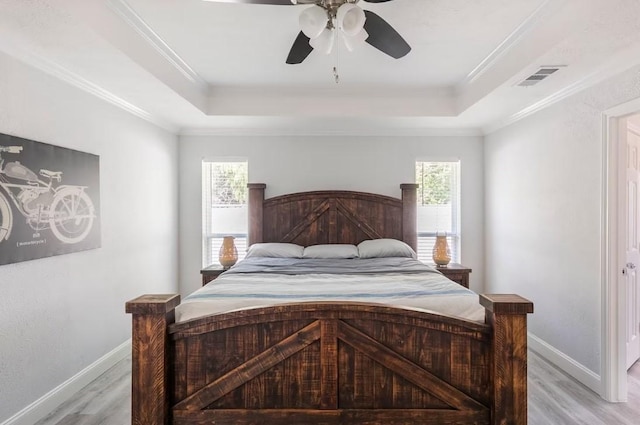 bedroom featuring light hardwood / wood-style floors, a tray ceiling, crown molding, and ceiling fan