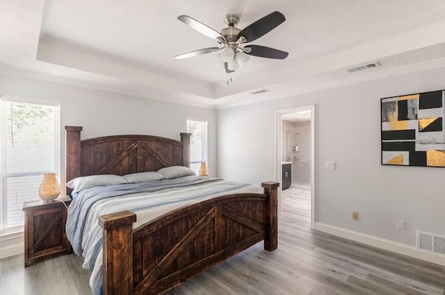 bedroom featuring a tray ceiling, ceiling fan, ensuite bathroom, and hardwood / wood-style flooring