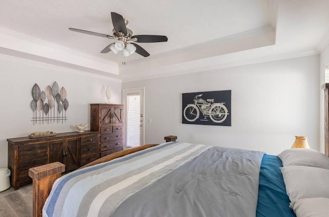 bedroom featuring ceiling fan, ornamental molding, wood-type flooring, and a tray ceiling