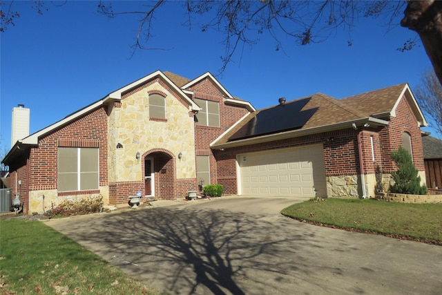 traditional home featuring driveway, a chimney, an attached garage, solar panels, and brick siding