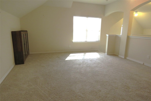 additional living space featuring arched walkways, carpet flooring, lofted ceiling, and baseboards