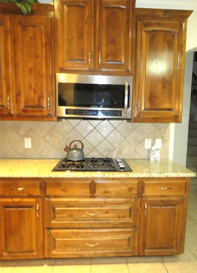 kitchen with tasteful backsplash, black gas cooktop, light stone countertops, and light tile patterned floors