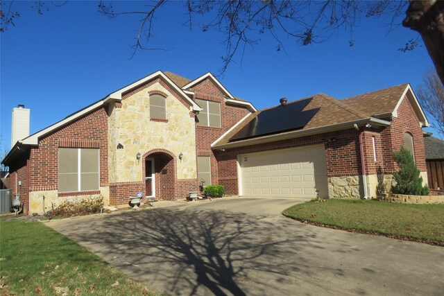 view of front of house featuring a garage, a front lawn, and solar panels