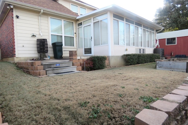 rear view of property with a lawn, roof with shingles, and a sunroom