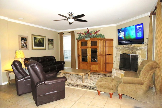 living area featuring light tile patterned floors, ceiling fan, crown molding, a stone fireplace, and baseboards