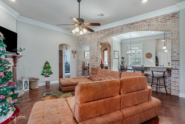 living room featuring crown molding, ceiling fan with notable chandelier, dark hardwood / wood-style floors, and brick wall