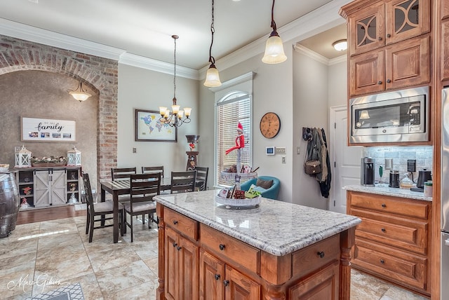 kitchen with pendant lighting, stainless steel microwave, light stone counters, ornamental molding, and a kitchen island