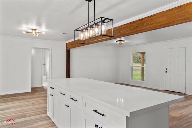 kitchen featuring white cabinetry, a center island, light stone counters, ornamental molding, and decorative light fixtures