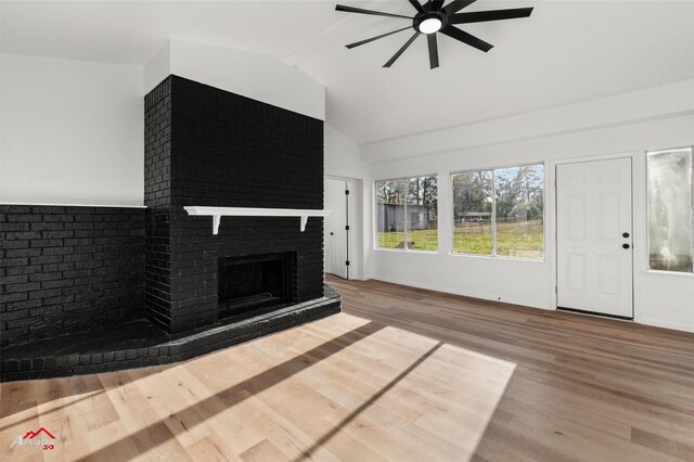 unfurnished living room with ceiling fan, hardwood / wood-style floors, vaulted ceiling, and a brick fireplace