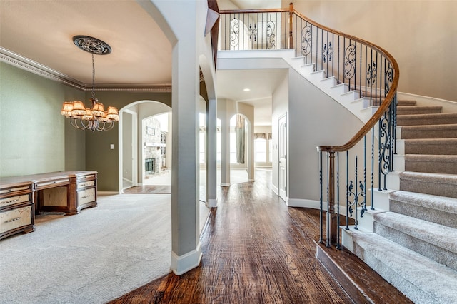 entryway with hardwood / wood-style flooring, ornamental molding, a towering ceiling, and an inviting chandelier