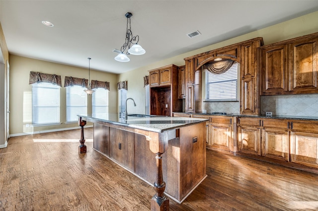 kitchen with a center island with sink, plenty of natural light, dark hardwood / wood-style flooring, and dark stone counters