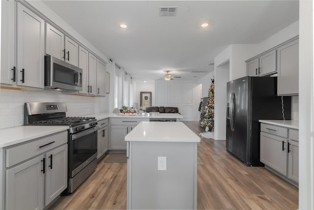 kitchen with gray cabinetry, a center island, stainless steel appliances, and hardwood / wood-style flooring