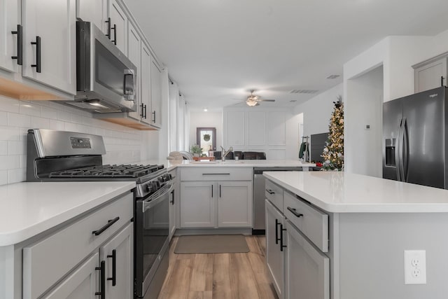 kitchen featuring kitchen peninsula, appliances with stainless steel finishes, backsplash, ceiling fan, and gray cabinets