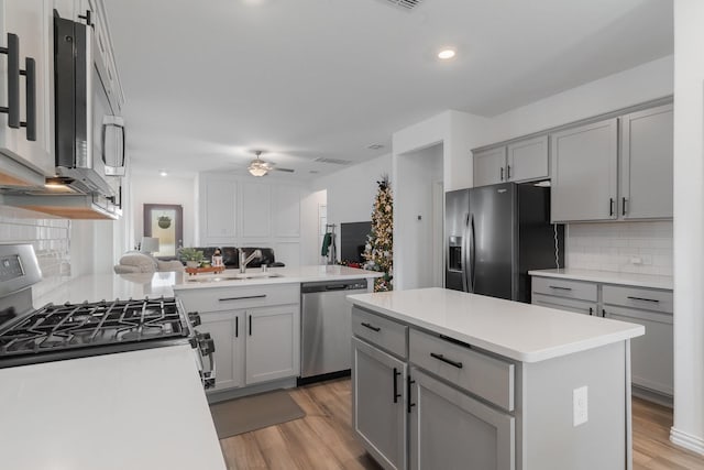 kitchen featuring sink, tasteful backsplash, gray cabinets, a kitchen island, and appliances with stainless steel finishes