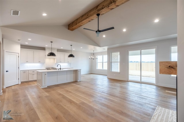 kitchen featuring decorative light fixtures, beamed ceiling, white cabinets, a kitchen island with sink, and light hardwood / wood-style flooring