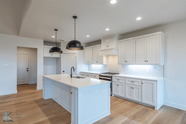 kitchen with white cabinetry, sink, stainless steel range with gas cooktop, and an island with sink