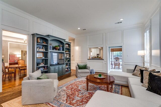 living room with built in shelves, light hardwood / wood-style floors, and crown molding