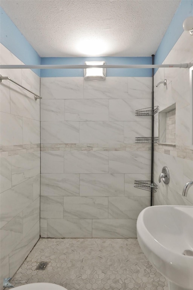 bathroom featuring tile patterned floors, sink, toilet, a textured ceiling, and a tile shower