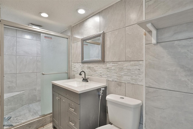 bathroom with a textured ceiling, toilet, a shower with door, vanity, and tile walls