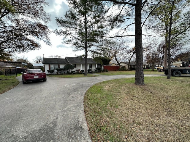 view of front of property with fence, curved driveway, and a front lawn