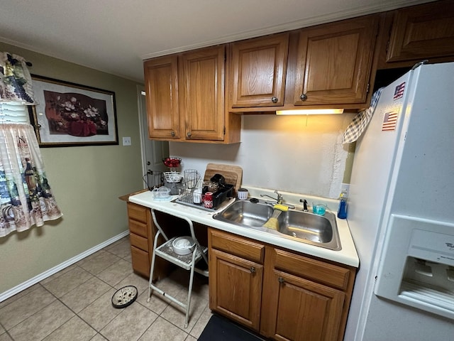 kitchen featuring light tile patterned floors, light countertops, brown cabinetry, a sink, and white fridge with ice dispenser