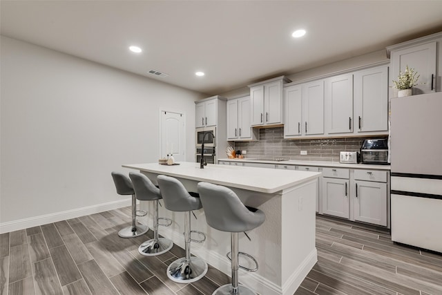 kitchen with decorative backsplash, built in microwave, a kitchen island with sink, white fridge, and a breakfast bar area