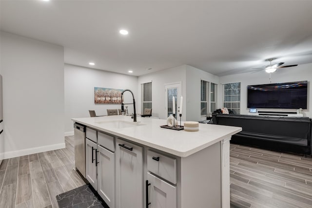 kitchen with stainless steel dishwasher, ceiling fan, a kitchen island with sink, sink, and white cabinets