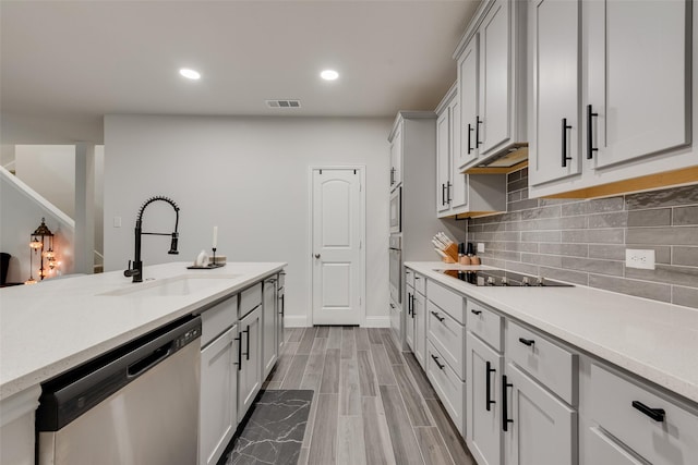 kitchen featuring appliances with stainless steel finishes, light wood-type flooring, tasteful backsplash, and sink