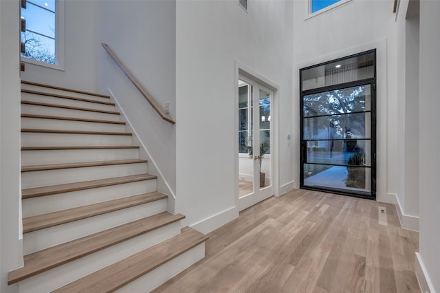 foyer featuring a healthy amount of sunlight, light hardwood / wood-style floors, a high ceiling, and french doors