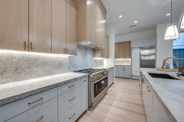 kitchen with light brown cabinetry, sink, light hardwood / wood-style flooring, high quality appliances, and hanging light fixtures