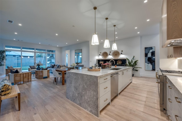 kitchen with light wood-type flooring, stainless steel appliances, decorative light fixtures, a center island with sink, and white cabinetry