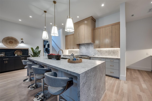 kitchen featuring pendant lighting, backsplash, light hardwood / wood-style flooring, an island with sink, and a breakfast bar area