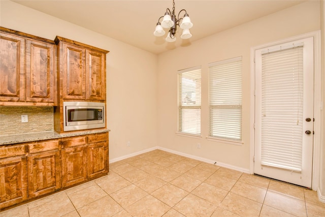 kitchen featuring light stone countertops, stainless steel microwave, light tile patterned floors, and a chandelier